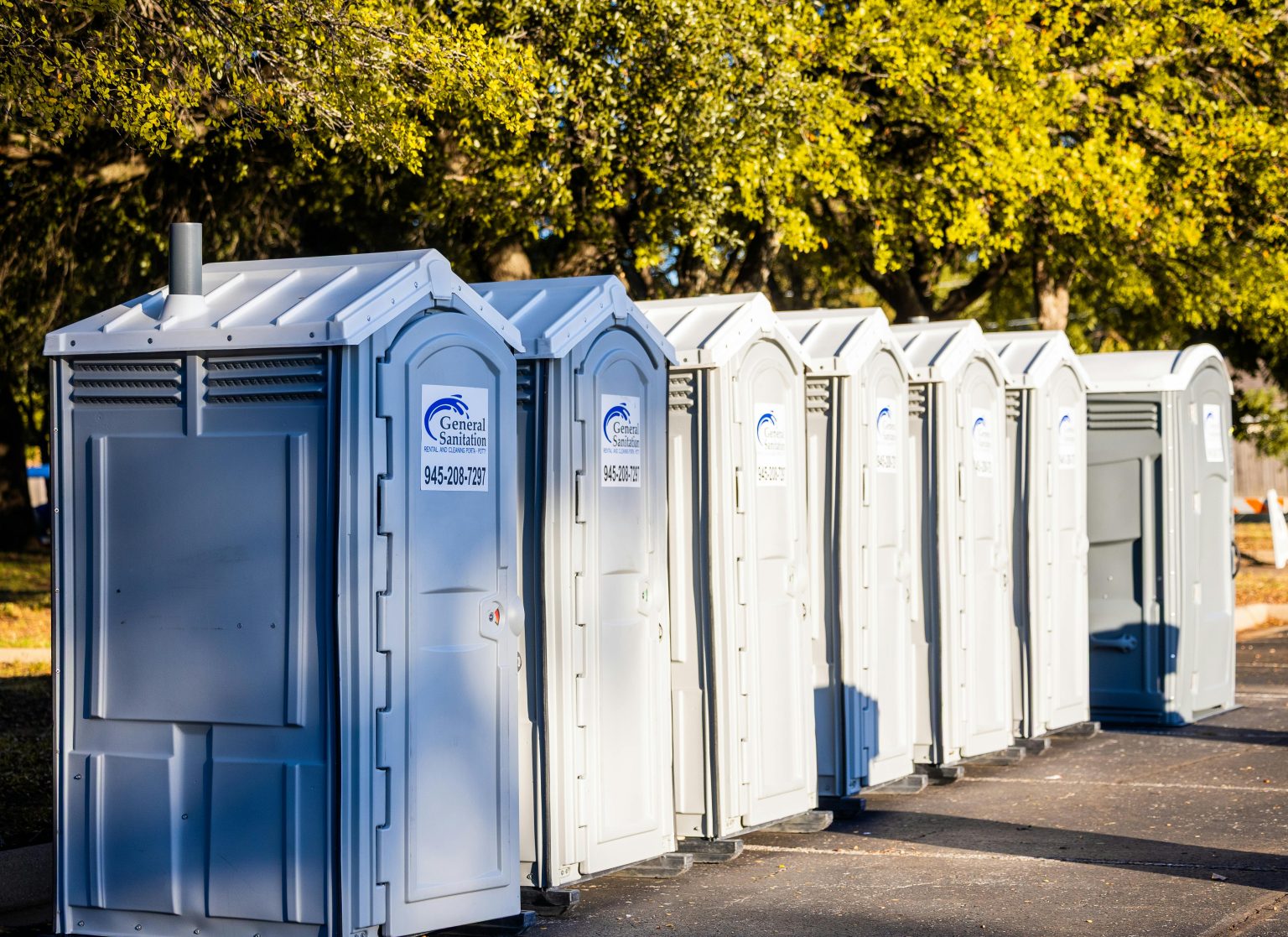 Multiple portable toilets aligned outdoors under trees, creating a sanitation solution.