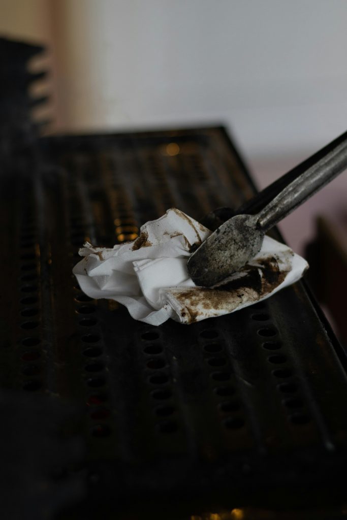 Close-up of tongs using a dirty tissue to clean a grill grate, emphasizing hygiene.