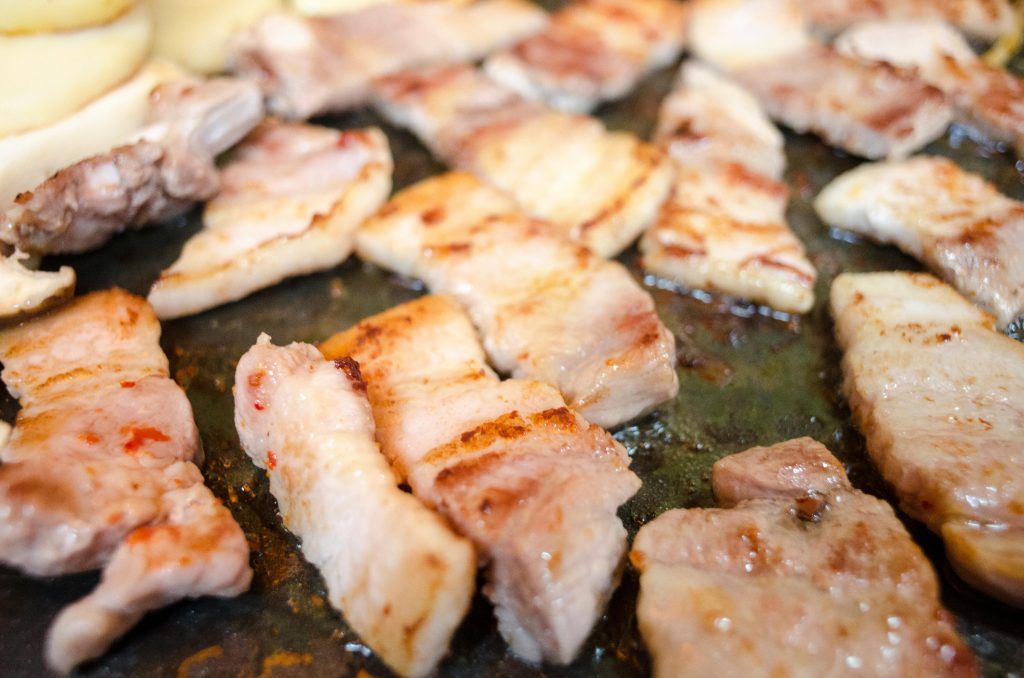 Juicy pork belly slices sizzling on a hot grill, capturing the essence of grilling with visible oils and fat.