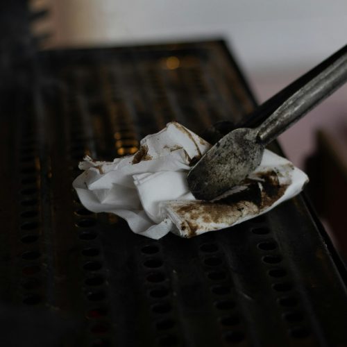 Close-up of tongs using a dirty tissue to clean a grill grate, emphasizing hygiene.